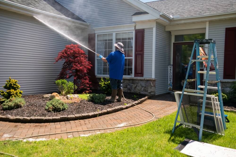 The Spotless Windows Sydney cleaner pressure washing the wall outside the house